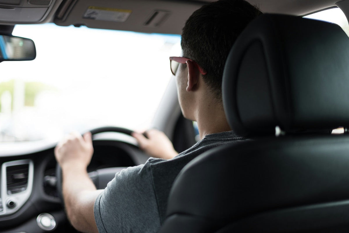 A young driver behind the wheel seen from the back seat